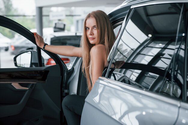 Opening the door. Girl and modern car in the salon. At daytime indoors. Buying new vehicle