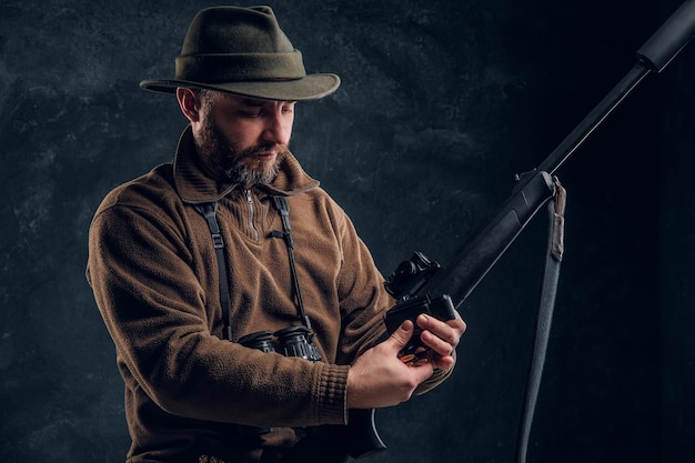 봄 사냥 시즌 개막. 사냥할 준비가 된 사냥꾼이 사냥용 소총을 충전하고 있습니다. 어두운 벽 배경 스튜디오 사진