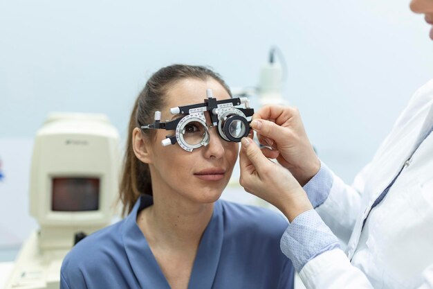 眼科医は、眼科クリニックで視力をチェックするために検眼医のトライアルフレームの女性患者と女性を検査します