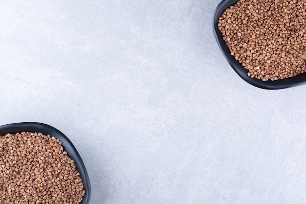 Free photo opposingly arranged bowls of raw buckwheat on marble surface