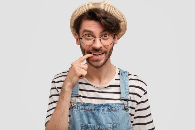 Optimistic cheerful bearded male farmer bites index finger