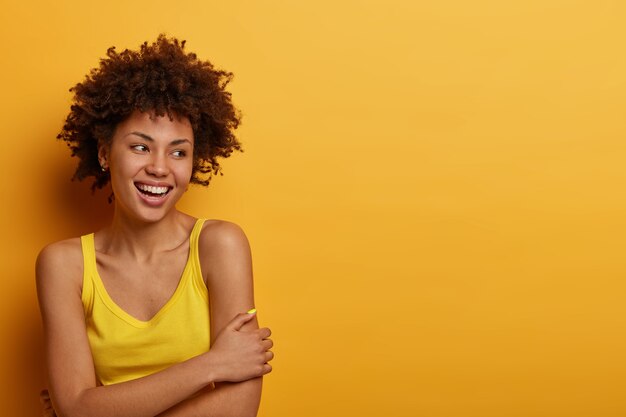 Optimistic glad millennial girl crosses hands, stands shy and expresses positive feelings