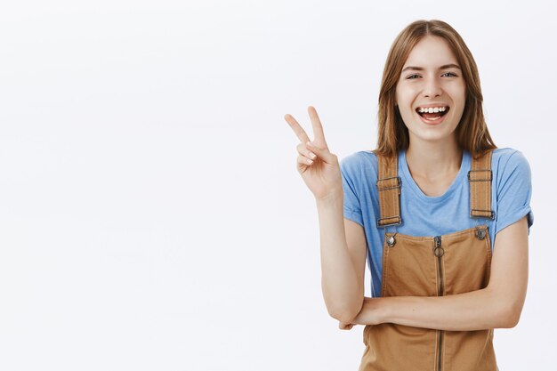 Optimistic happy attractive girl showing peace gesture and laughing