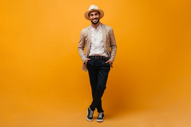 Optimistic man in black pants and beige jacket posing on orange background