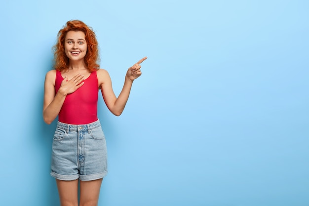楽観的な見栄えの良い赤い髪の若い女性は、自由空間に前指を指します