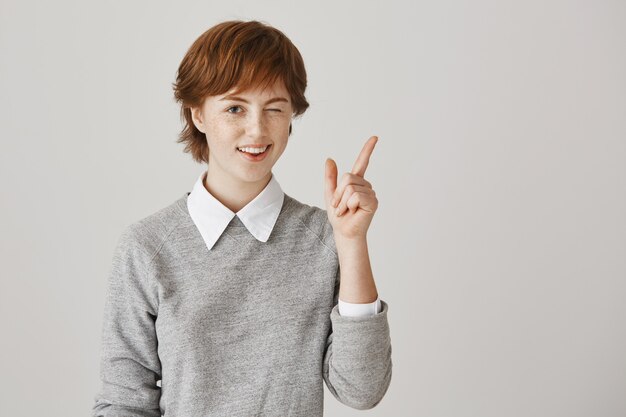 Optimistic redhead girl with short haircut posing against the white wall