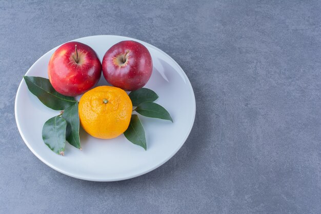 Orange and apples with leaves on plate on the dark surface