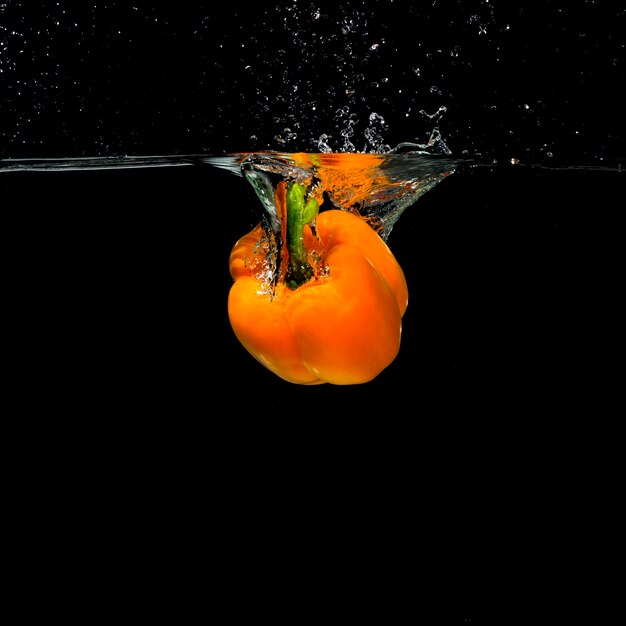 An orange bell pepper falling into the water on black background
