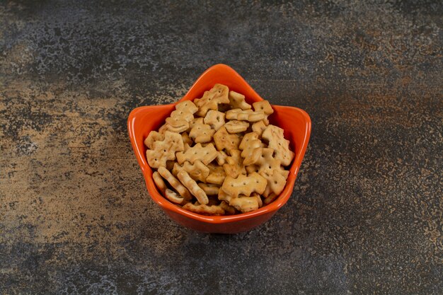 Orange bowl of crackers on marble.