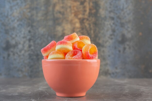 Orange bowl full with colorful candies on grey surface.