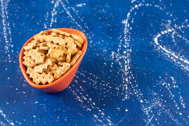 Foto gratuita ciotola arancione di piccoli cracker salati sulla superficie di marmo