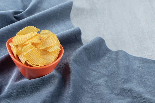 Orange bowl of tasty ripple chips on stone.