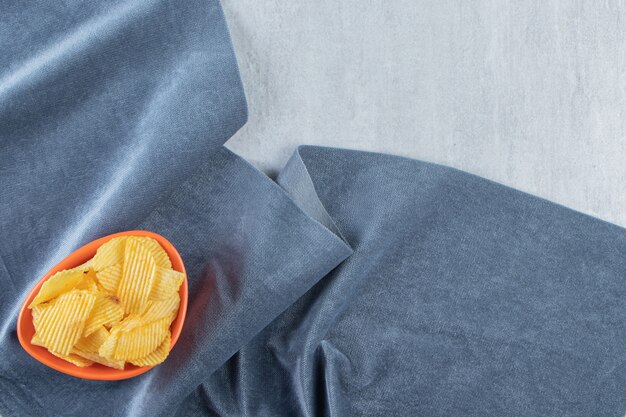 Orange bowl of tasty ripple chips on stone.