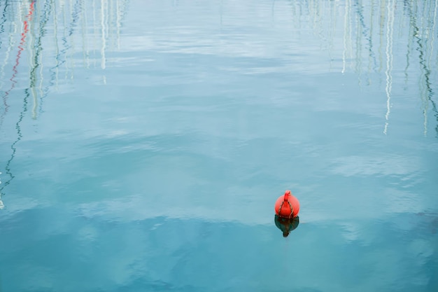 Free photo orange buoy floating on the waves of the sea surface in the bay reflection of yacht masts in the water the concept of the safety of human life