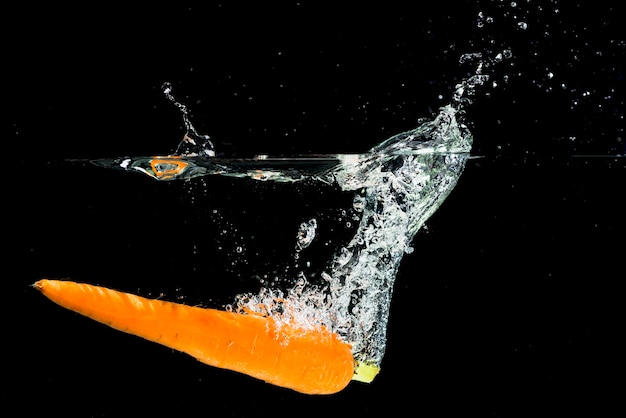 An orange carrot falling into water splash over black background