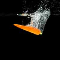 Free photo an orange carrot falling in water splash against black background