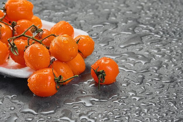 물에 있는 오렌지 체리 토마토는 회색 테이블에 떨어집니다. 복사 공간이 있는 어두운 스타일 근접 촬영 샐러드 또는 야채 선택에 초점을 맞춘 요리
