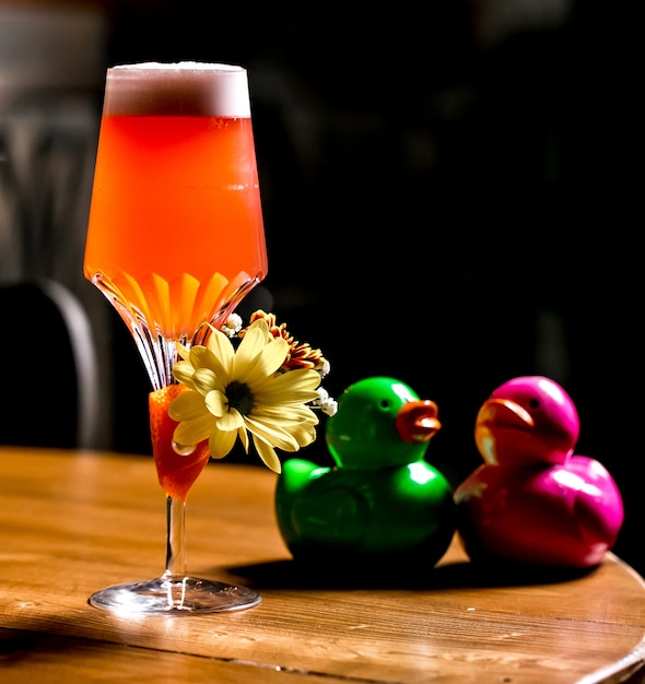 Orange cocktail garnished with flower placed next to crystal ducks