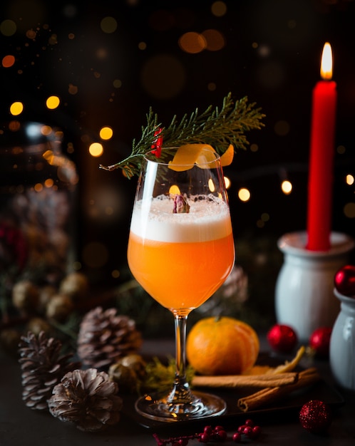 Orange cocktail with christmas cones, lights and red candle.