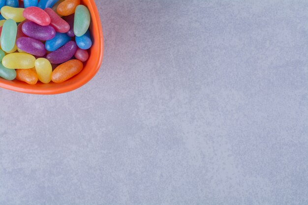 An orange deep plate full of colorful bean candies on gray surface