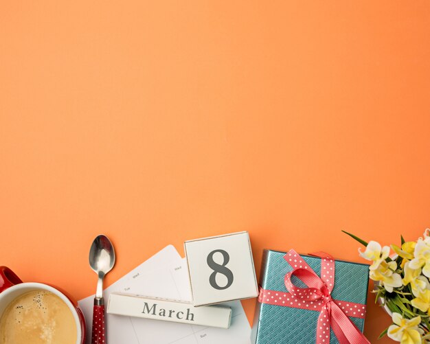 Orange desk with cup of coffee, gift, flowers and notebook