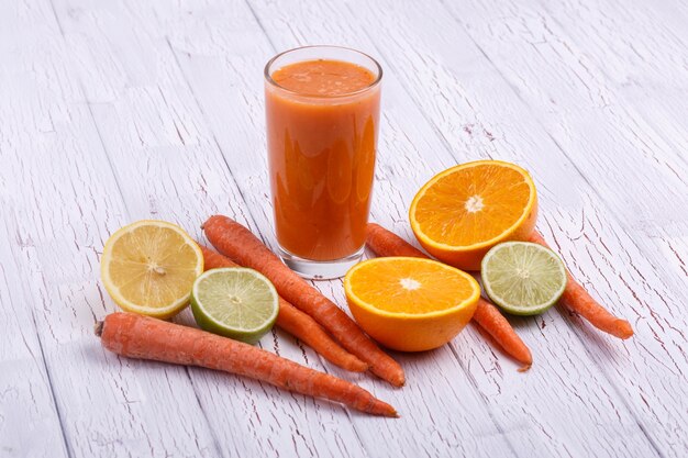 orange detox coctail with oranges and carrots lies on white table