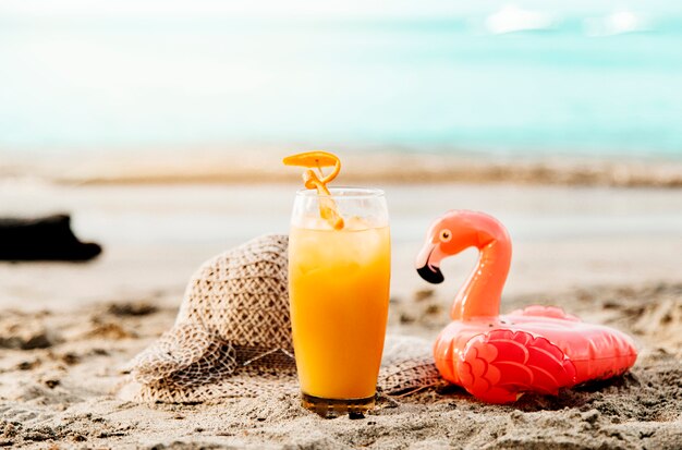 Orange drink and toy flamingo on sand