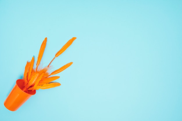 Free photo an orange feathers spilling from the plastic glass on blue background