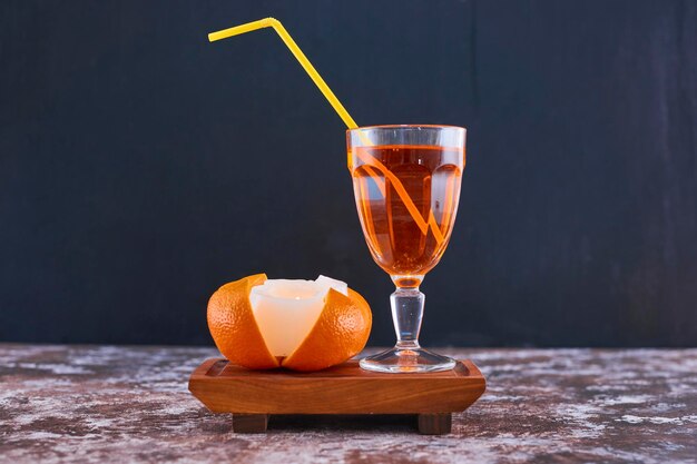 Orange and a glass of juice with yellow pipe on wooden platter on the marble in the middle. High quality photo
