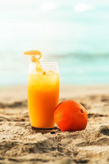 Апельсин и стакан с соком на песчаном пляже