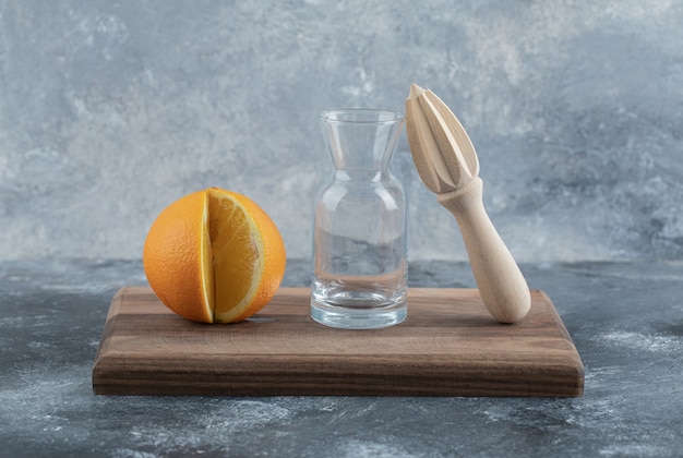 Orange, glass and wooden reamer on wooden board. 