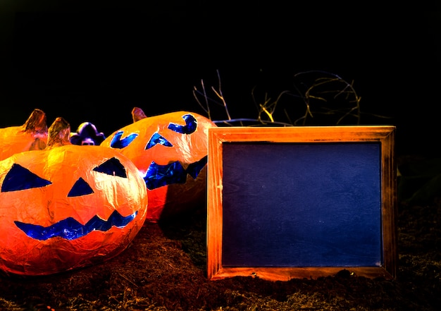 Foto gratuita zucche fatte a mano arancio nello stile di halloween con i fronti intagliati che si trovano accanto alla struttura vuota della foto