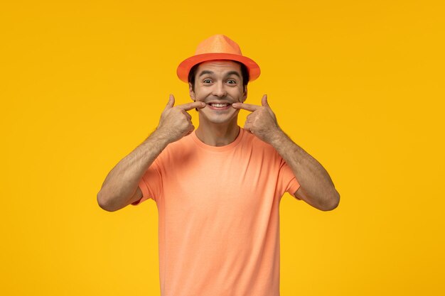 彼の顔に笑顔で指で指している帽子とオレンジ色のTシャツのオレンジ色の帽子かわいい若い男