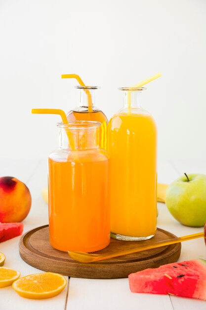 Бутылки апельсинового сока с трубочкой на деревянный поднос с фруктами на деревянный стол