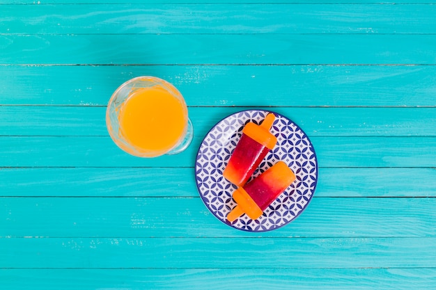 Foto gratuita succo d'arancia e popsicle di frutta luminosa sul piatto su superficie di legno