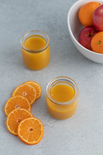 Orange juice in clear glass jar near sliced oranges and orange and apple fruits in round bowl