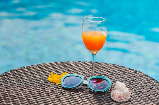 Orange juice and sunglasses with swimming pool background