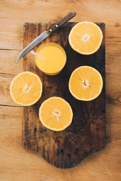 An orange juice with halved orange and knife on chopping board against wooden backdrop