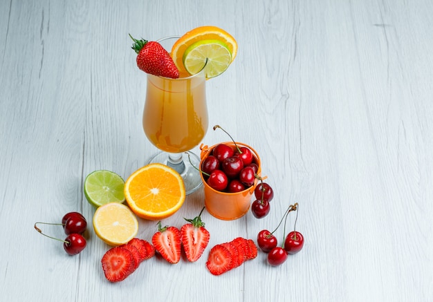 Succo d'arancia con limone, lime, arancia, fragola, ciliegia in un calice su superficie di legno, vista di alto angolo.