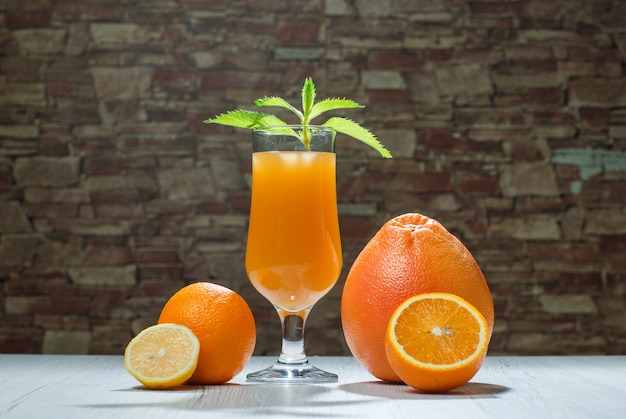 木製とレンガの石の背景、側面図のゴブレットでミント、柑橘系の果物とオレンジジュース。