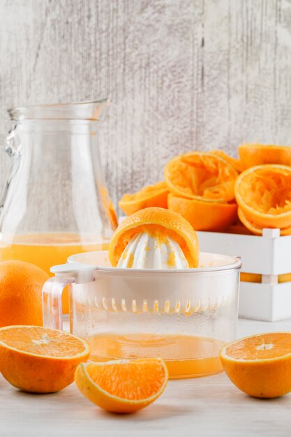 Orange juice with oranges, squeezer in a jug on white surface