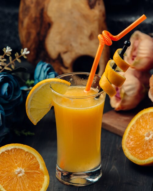 Апельсиновый сок с ломтик и красная труба в стакане.
