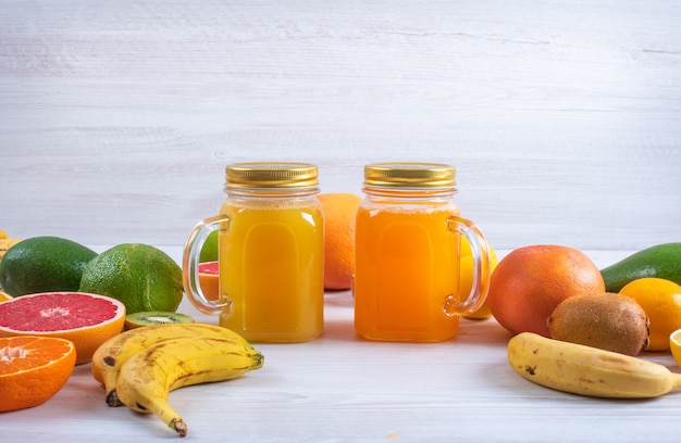 Orange and lemon juice surrounded by different colorful fresh citrus fruits on white table