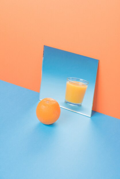 Orange near juice in mirror on blue table isolated