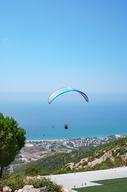 Orange paraglider flies over a mountain valley on a sunny summer day.