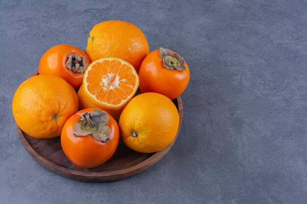 Orange and persimmon on wooden plate on marble table.