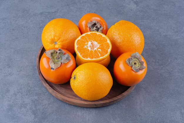 대리석 테이블에 있는 나무 접시에 오렌지와 감.