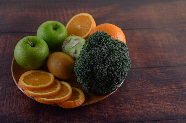 Orange pieces, apple, kiwi, and Broccoli on a wooden plate.