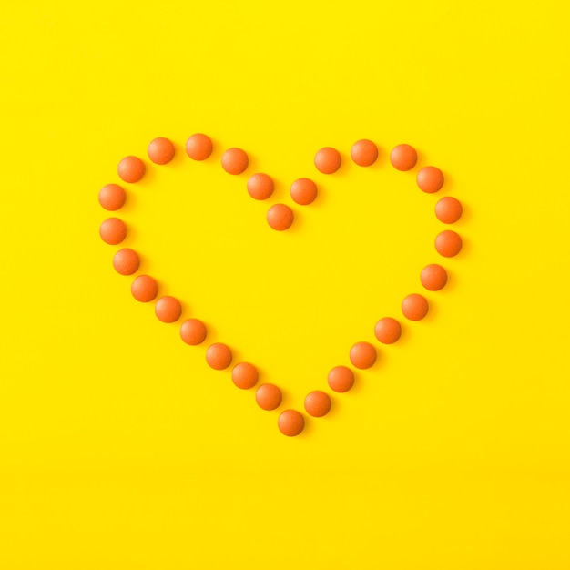 An orange pills forming heart shape on yellow background