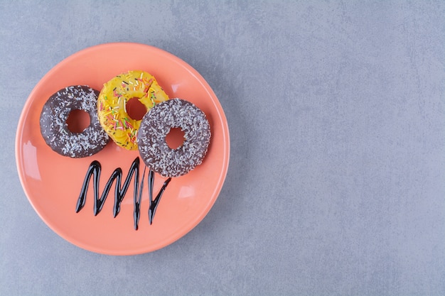 An orange plate of delicious chocolate doughnuts with sprinkles. 